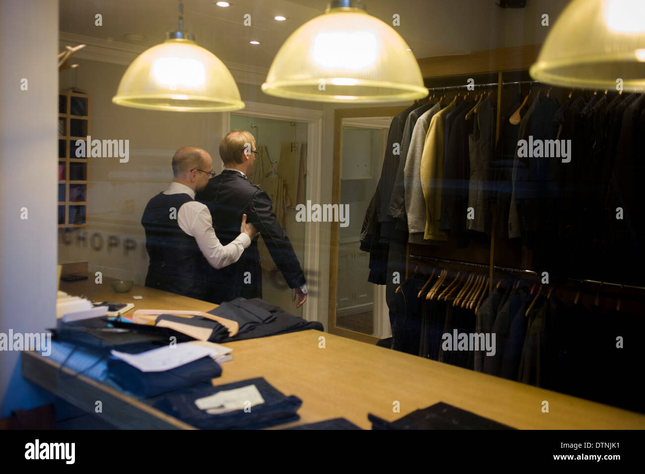 A gentleman client has a fitting for a new made-to-measure suit, seen through a City taylor's window. Stock Photo