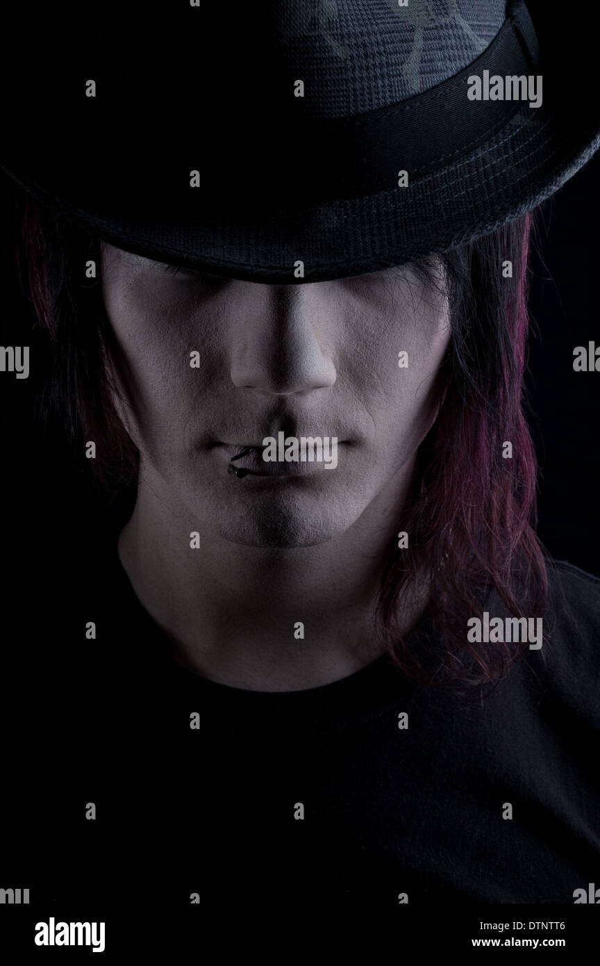 A gothic man wearing a Fedora hat, a moody headshot with black background Stock Photo