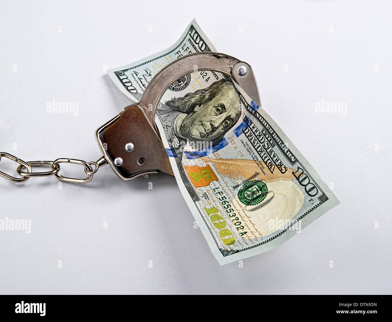 Cold hard cash in cold steel handcuffs. Stock Photo