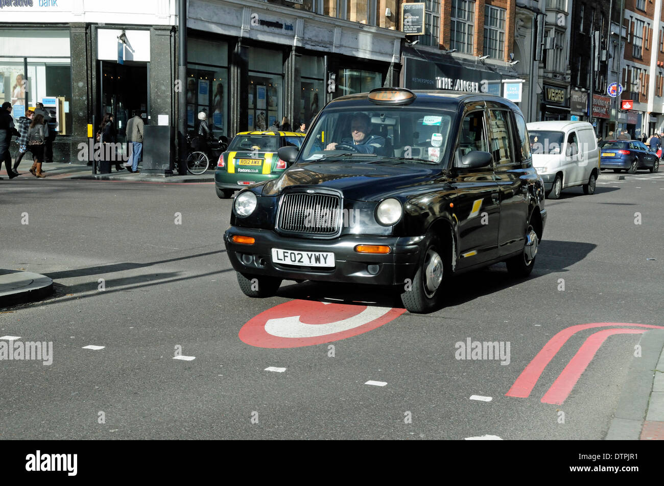 Black taxi cab entering congestion charge zone with C painted on road, Angel, Islington, London England UK Stock Photo