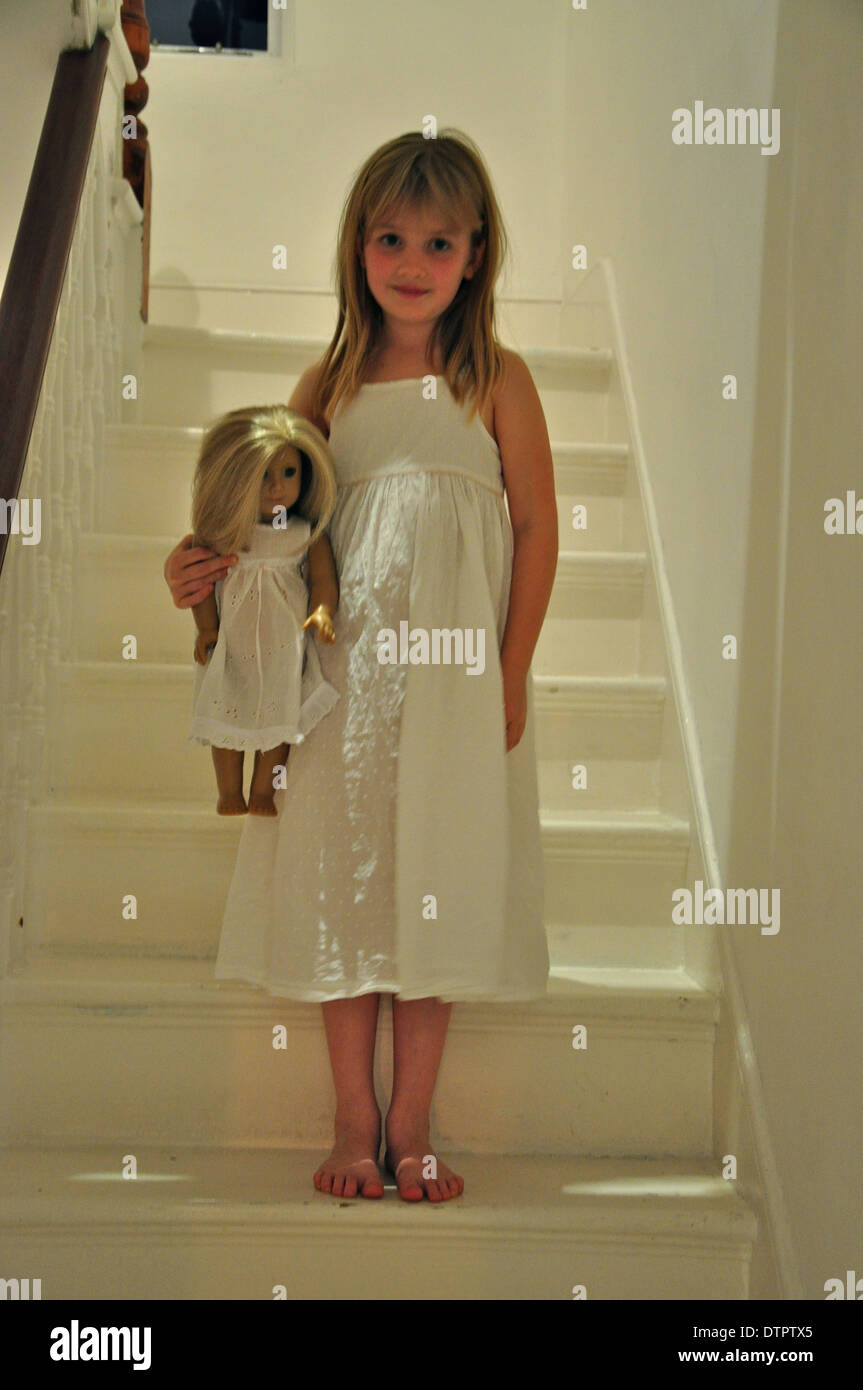 pretty little blonde girl dressed in white nightdress holding a doll getting ready for bedtime Stock Photo