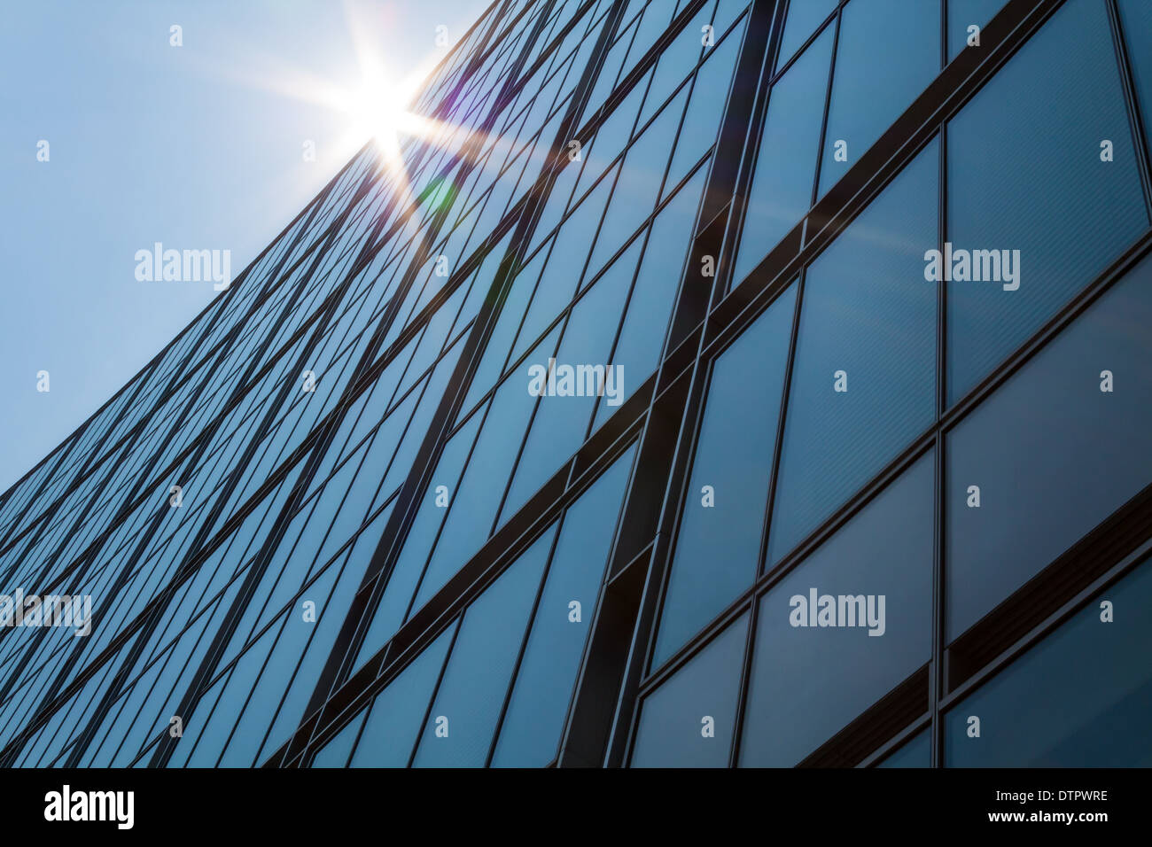 The sun shines over a tall glass fronted building. Stock Photo