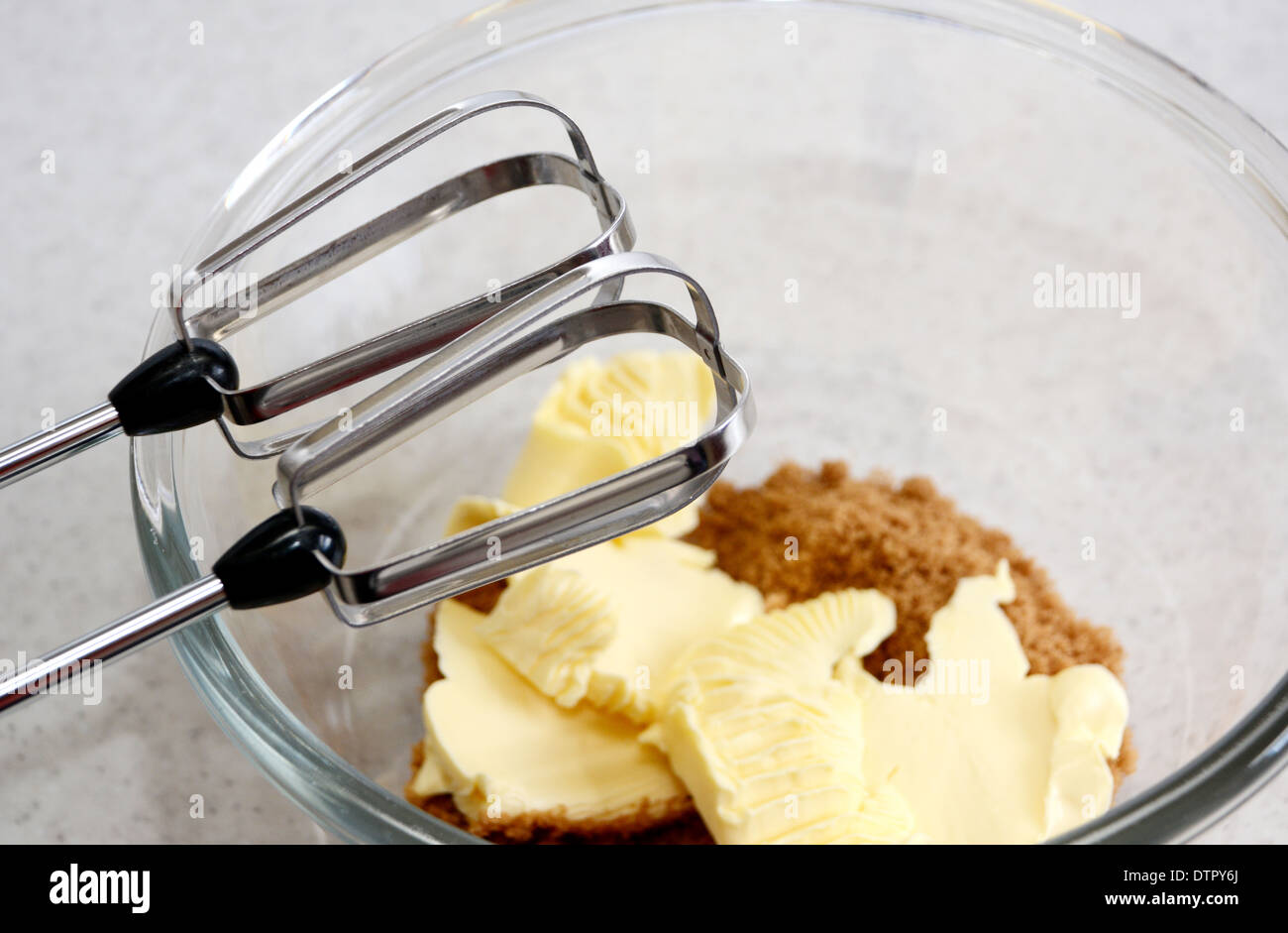 Electric whisk beaters above a glass bowl containing sugar and butter