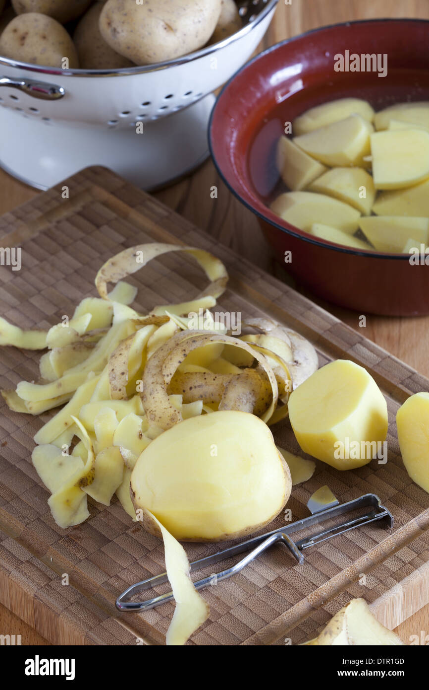 Cutting board with potatoes and potato peeler with colander and bowl in