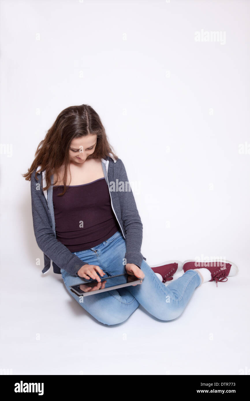 Young smiling female sitting using digital tablet, isolated on white background. Stock Photo