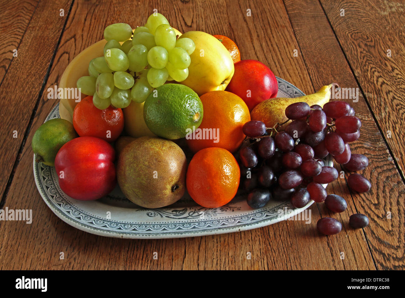Fresh fruit on a large retro plate, green grapes  black grapes pears limes apple nectarines Clementine's orange bananas Stock Photo