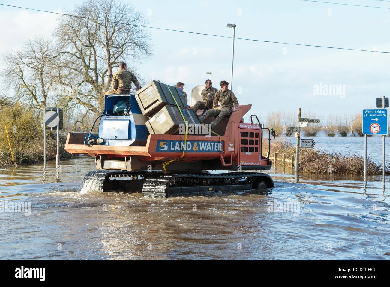 Burrowbridge, UK. 22nd Feb, 2014. Commandos helping at Burrowbridge on the flooded Somerset Levels on February 22, 2014. A group of soldiers are transported through the floodwater by workers of the Environment Agency in a Trac-dumper, a specialised vehicle capable of going through deep water. Supplies of oil and mechanical parts are sent to Saltmoor Pumping Station where water from Northmoor is being pumped into the tidal River Parrett to provide relief to the flooded area. These are the worst floods on the Somerset Levels in living history. Stock Photo