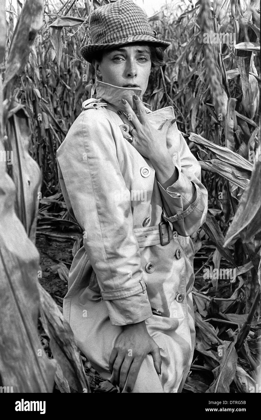 Sixties fashion model with raincoat and hat posing in a maize field Stock Photo