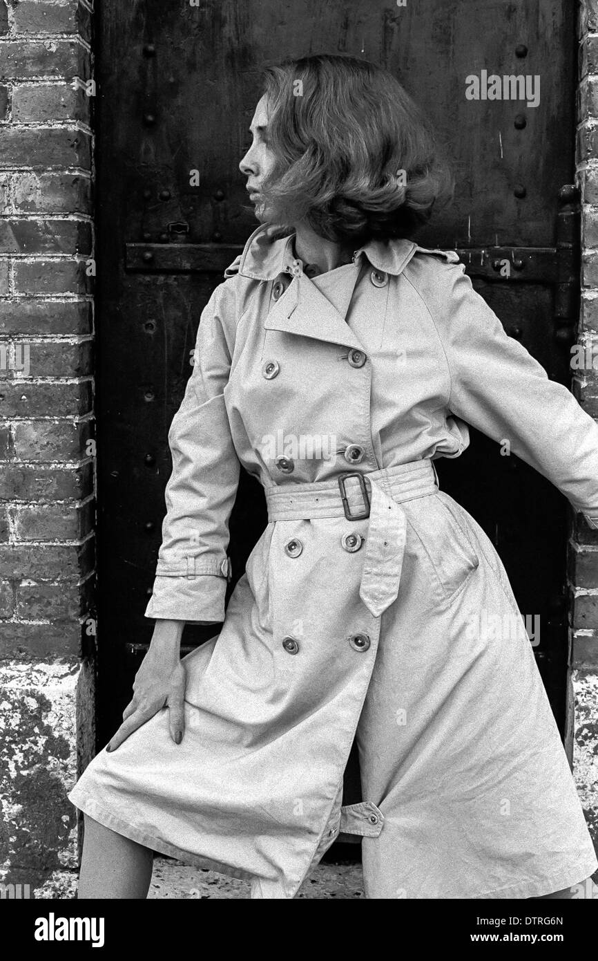 Sixties fashion model with raincoat posing against a black door Stock Photo