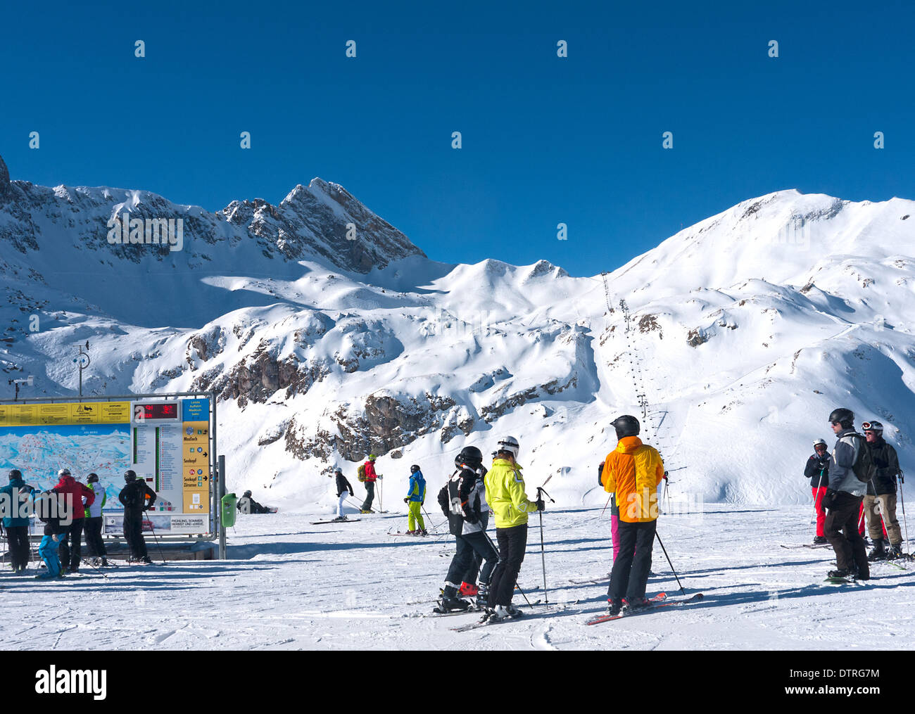 Skiers standing in the sun at Zurs - showing the link to Zug in the background, the Madloch lift by which you can access Lech. Stock Photo
