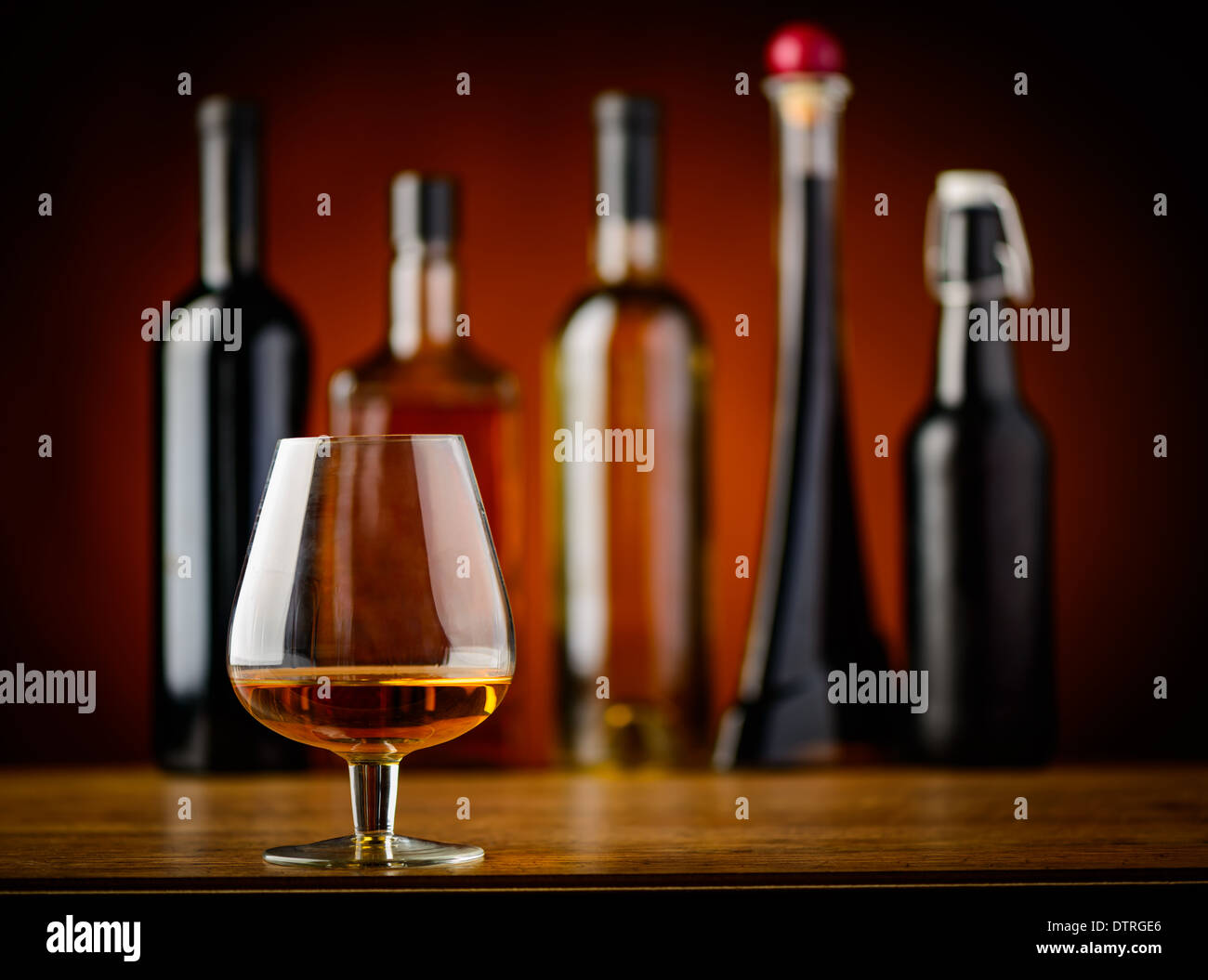 still life with glass of brandy and different bottles of alcohol drinks in background Stock Photo