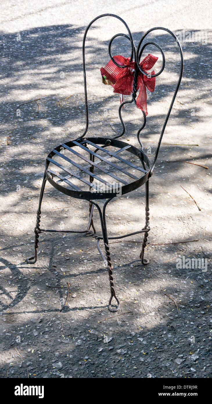 fanciful wire frame chair decorated with big red bow serves serving as humorous parking place saver outside boutique Oaxaca Stock Photo