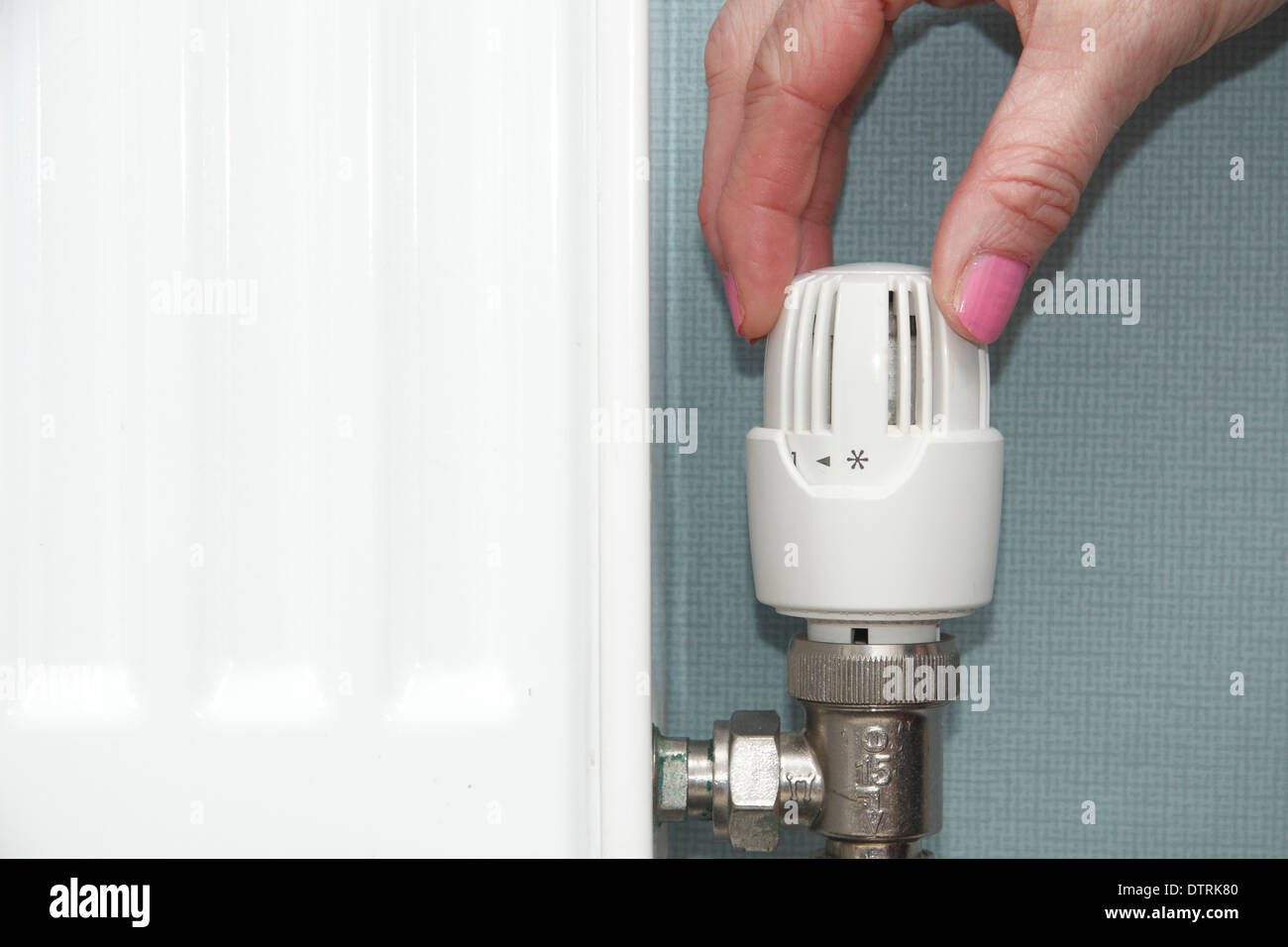 Woman turning thermostatic/radiator/ valve up/down on central heating system in domestic home, England, UK Stock Photo
