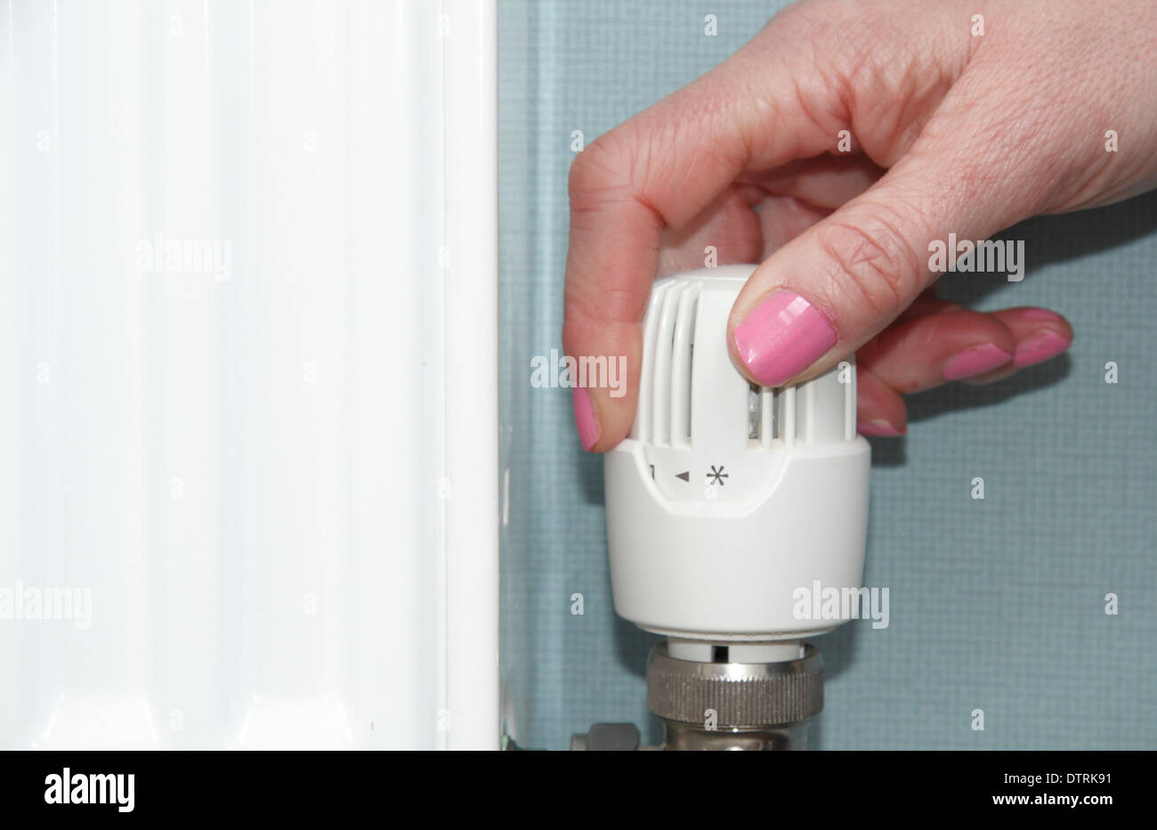 Woman turning thermostatic/radiator/ valve up/down on central heating system in domestic home, England, UK Stock Photo