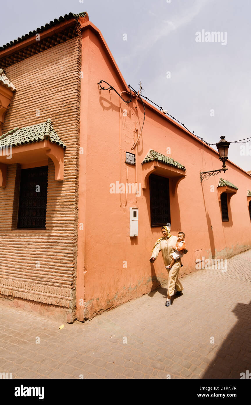 A woman walking carrying a child in the Medina of Marrakesh, Morocco. Stock Photo