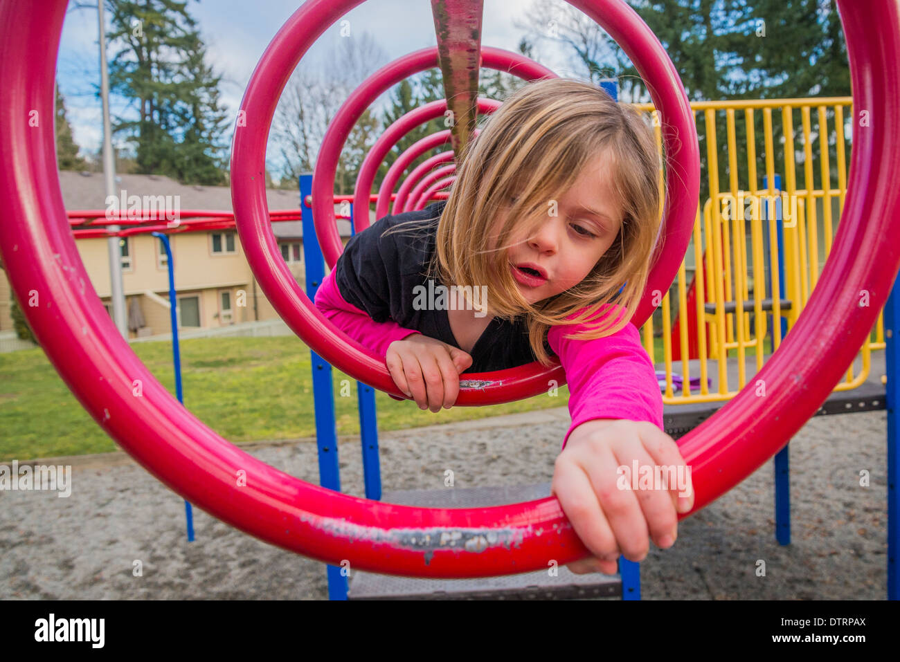 Young girl climbs through circular bars in playground Stock Photo