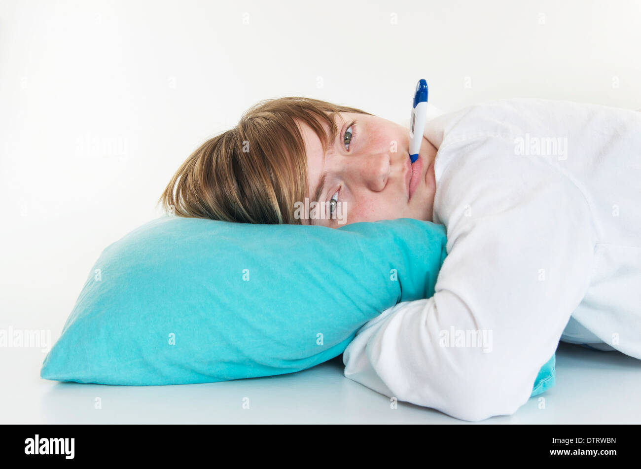 Sick young girl laying on pillow with thermometer in her mouth. Stock Photo