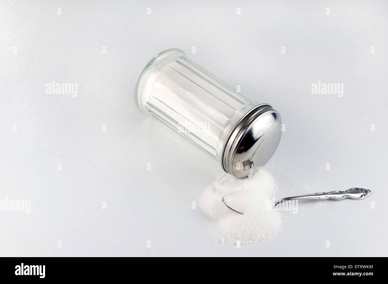 Sugar addiction. Tipped over sugar shaker or container spilling sugar onto spoon. Stock Photo