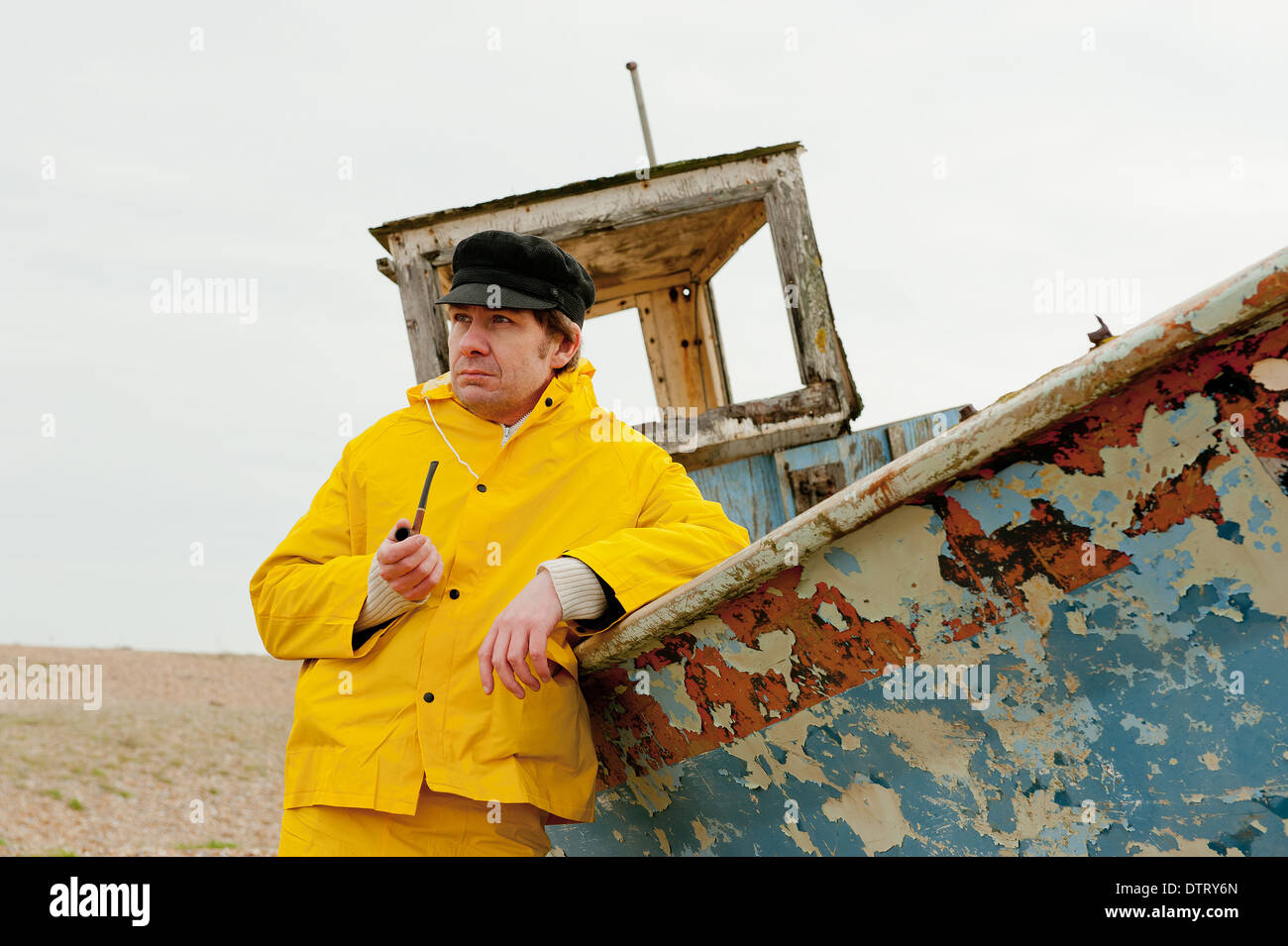 Fisherman in yellow waterproofs leaning against an old fishing boat and