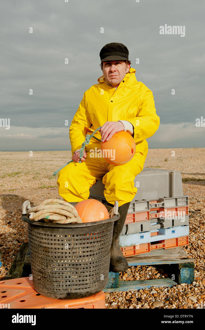 Fisherman sitting on plastic crates in his yellow water-proof clothing, getting ready his fishing equipment. Stock Photo