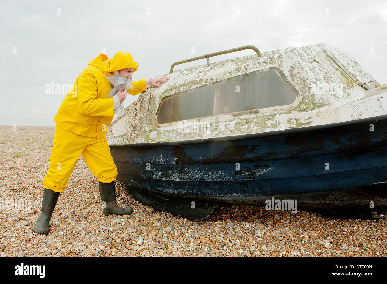 Fisherman in yellow water-proof overalls, checking for damage on an old boat. Stock Photo
