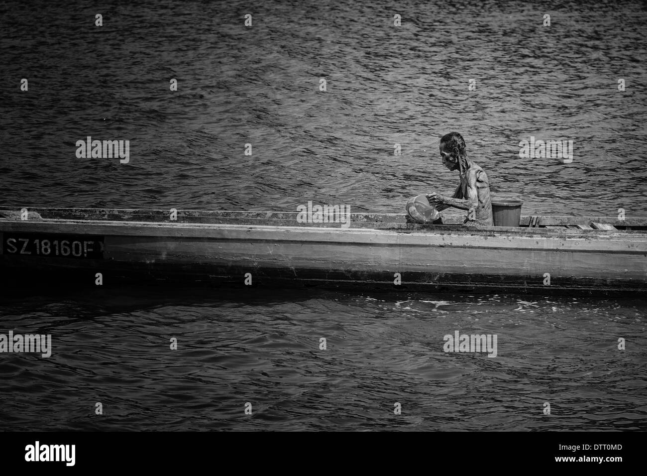 Black and White photo of a fisherman bailing water from his traditional sampan at St. John's Island, Singapore Stock Photo