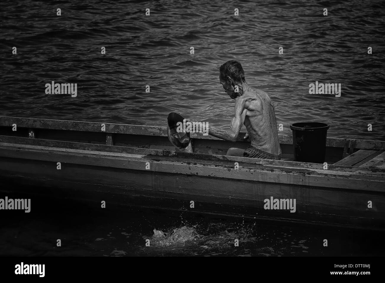 Black and White photo of a fisherman bailing water from his traditional sampan at St. John's Island, Singapore Stock Photo