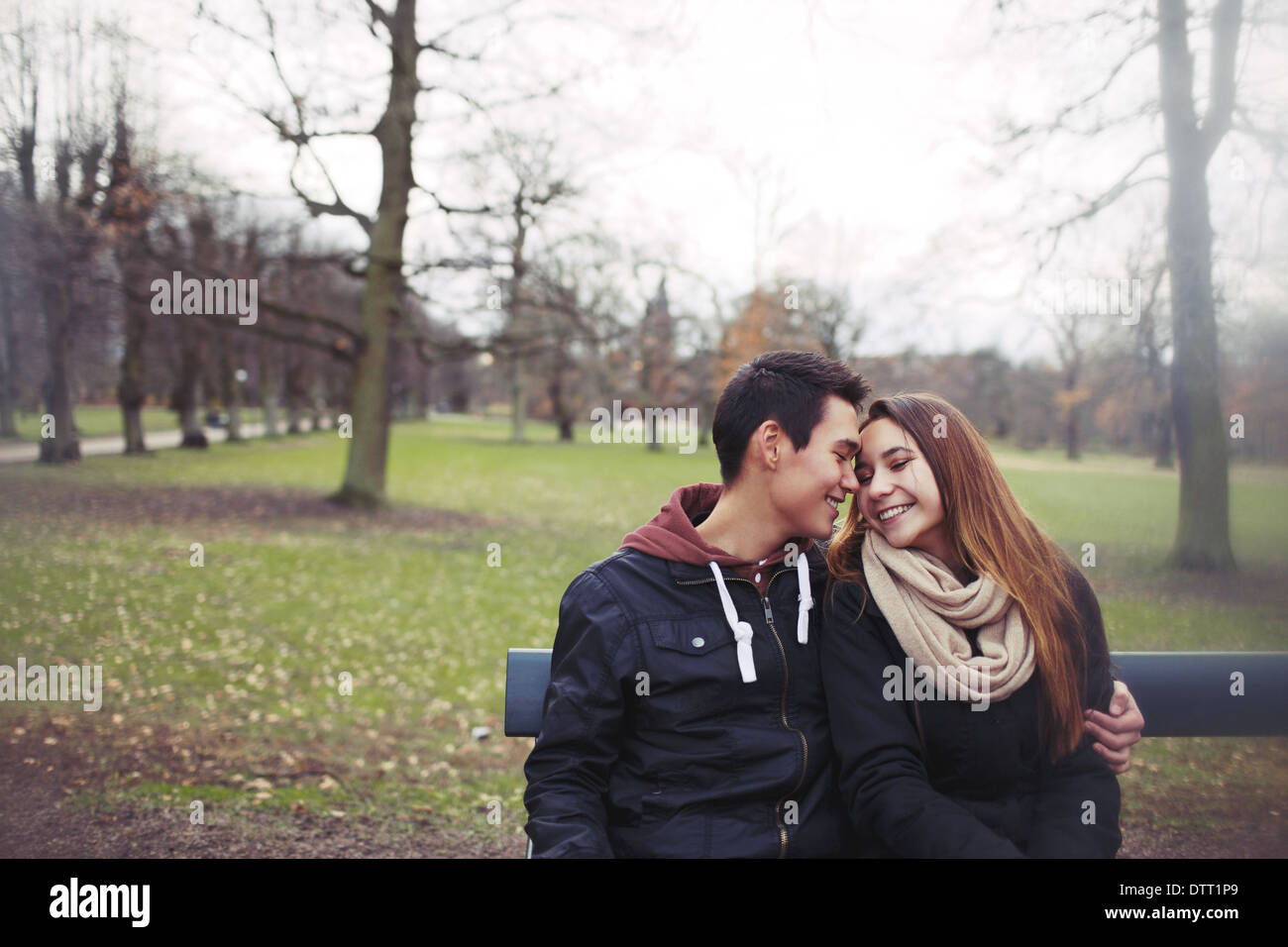 Romantic young couple sitting on a park bench outdoors in winter. Mixed ...