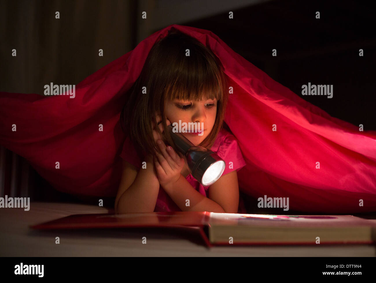 Caucasian girl reading by flashlight at night Stock Photo