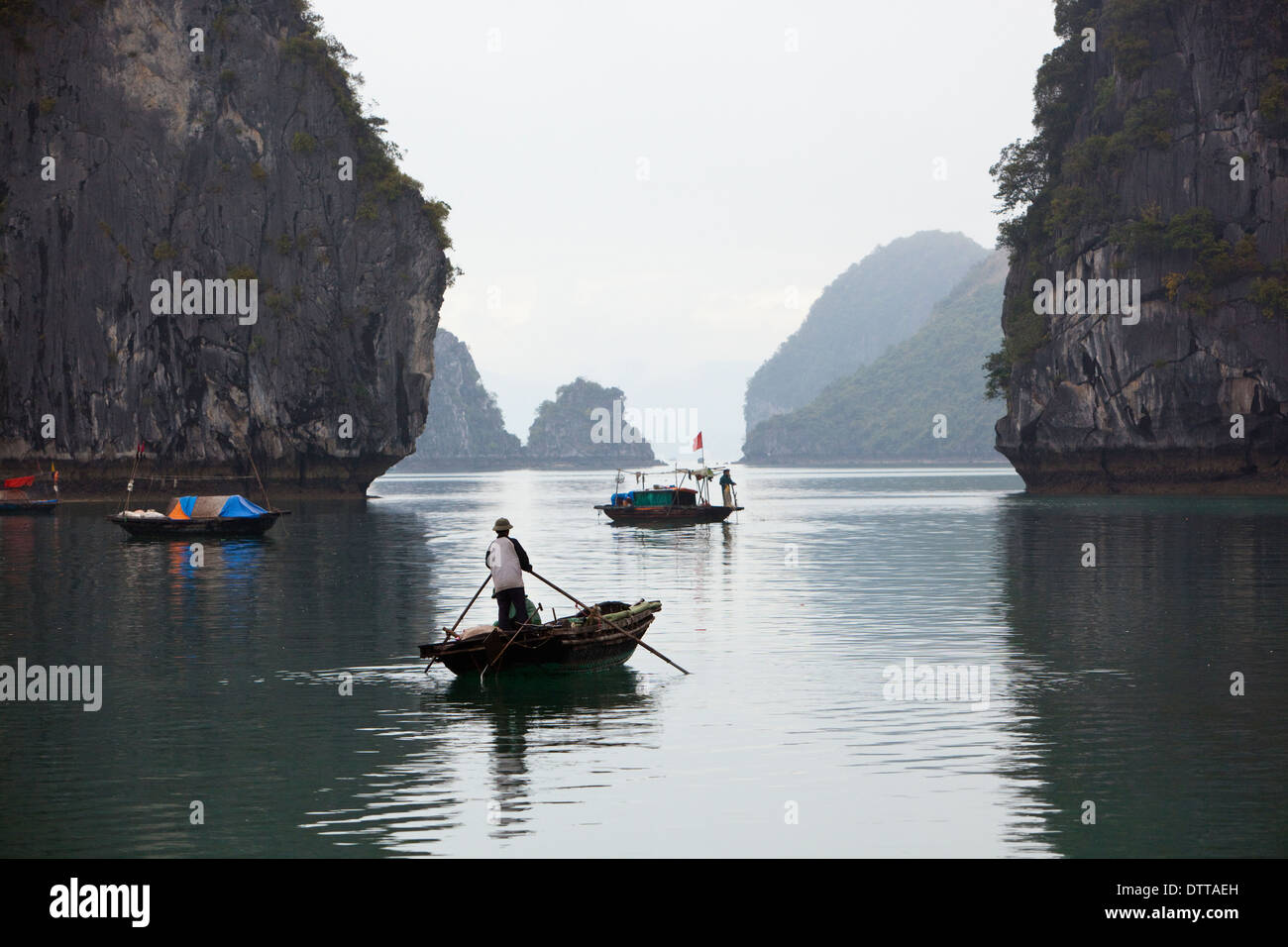 Two small fishing boats each with a man on, maneuver between tall rock outcrops in Ha Long Bay, Quang Ninh province, Vietnam Stock Photo