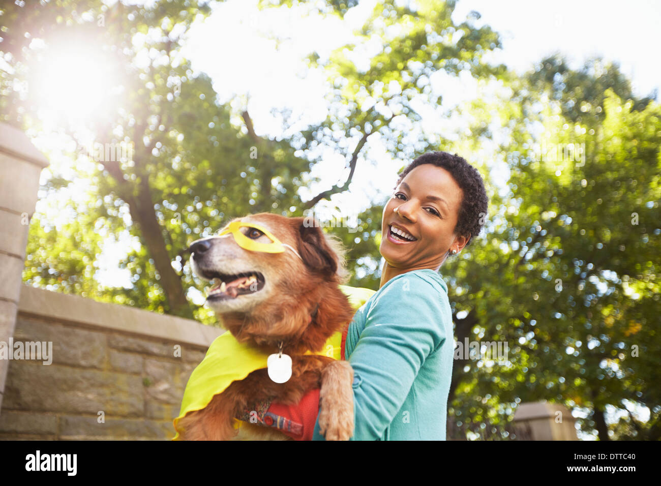Black woman carrying costumed dog in park Stock Photo