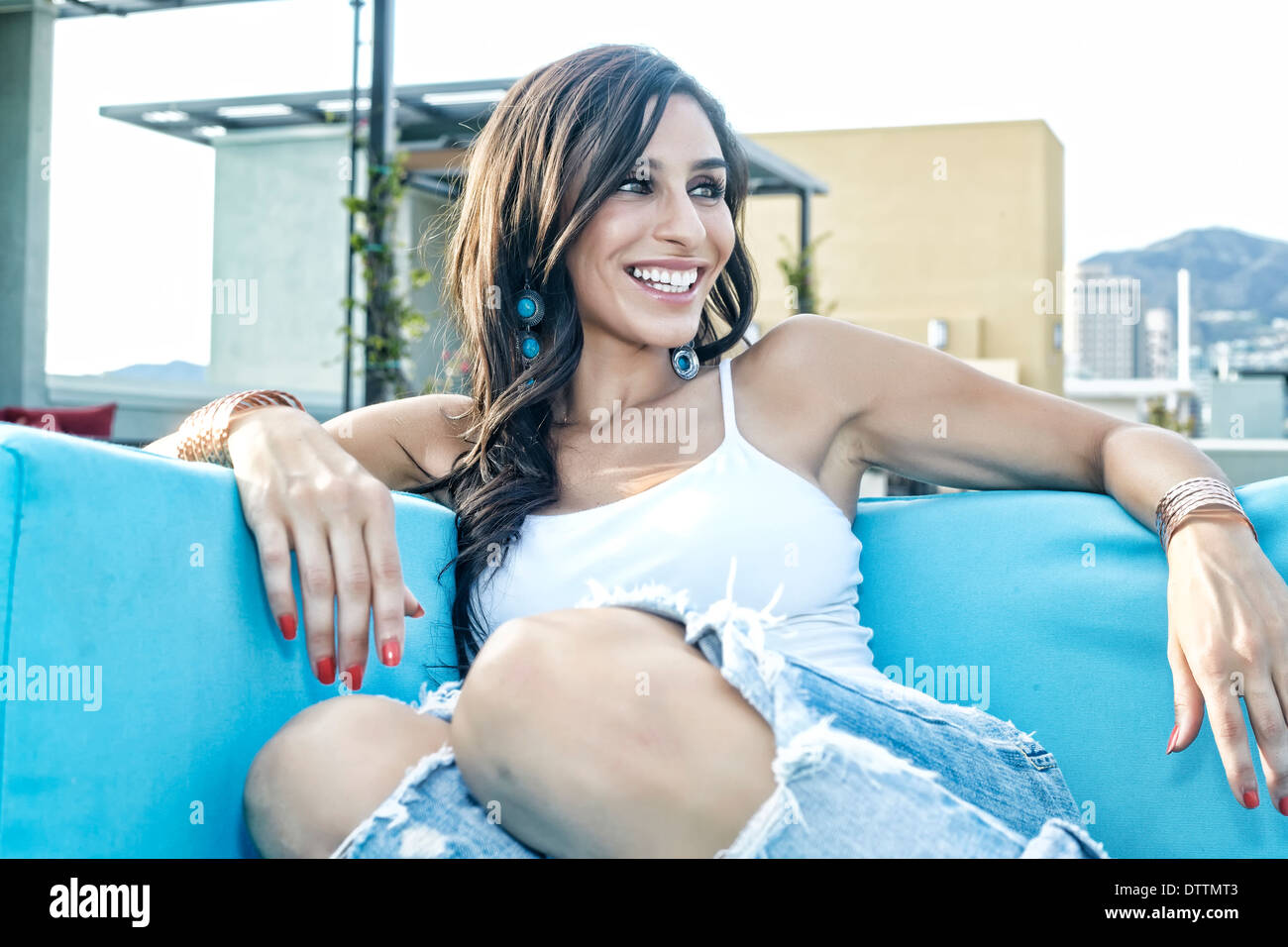 Middle Eastern woman relaxing on sofa on urban balcony Stock Photo