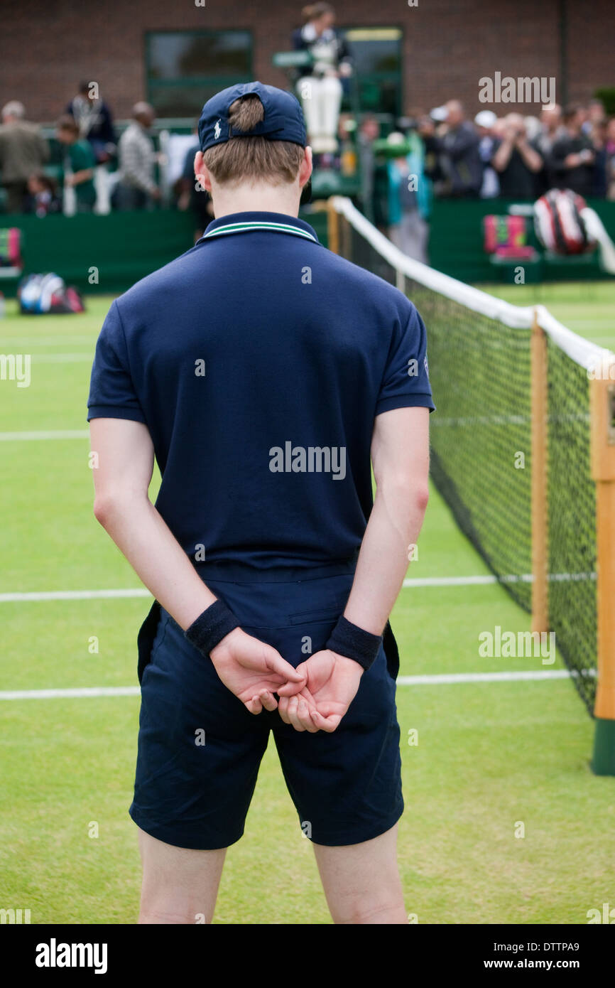 Back of Wimbledon tennis championship ball boy in foreground with net and umpire in background Stock Photo