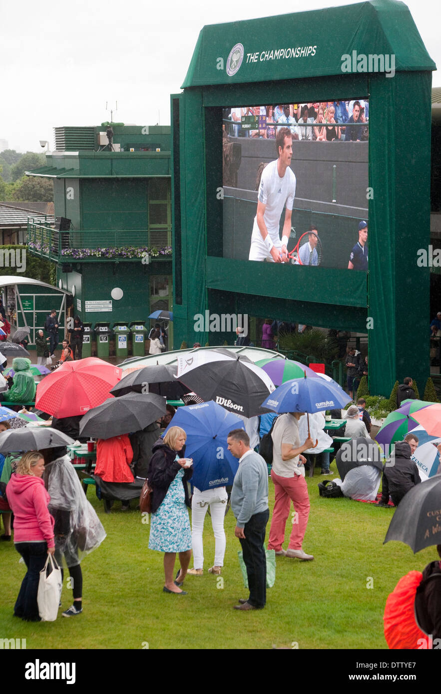 Wimbledon tennis crowd on Murray mount in background a TV screen showing Andy Murray foreground open Wimbledon umbrella Stock Photo