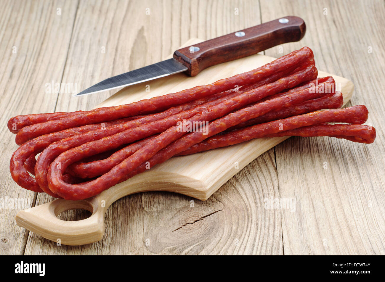 Lots of thin sausages and knife on a cutting board Stock Photo