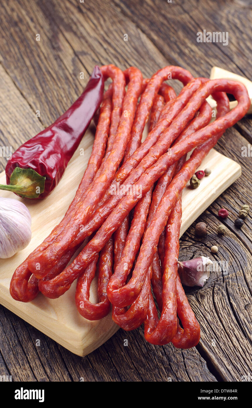 Thin dried sausages, pepper and garlic on old wooden table Stock Photo