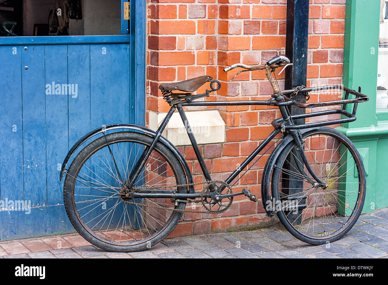 Old style bicycle bike chained to a drain pipe leaning against a red wall at Blists Hill Victorian Town Telford England Stock Photo