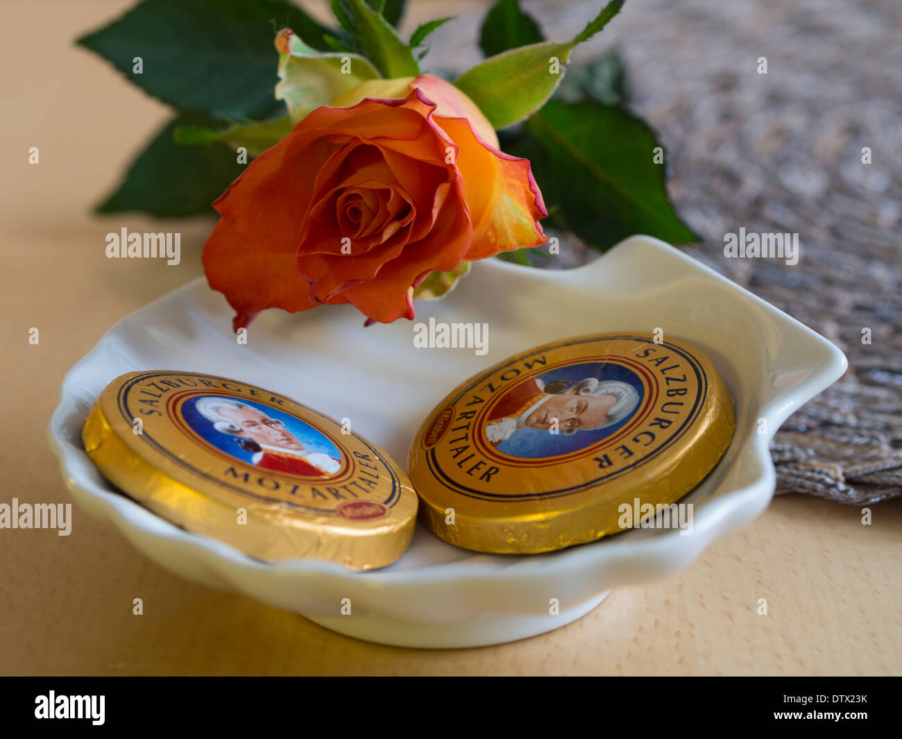 Two Mozarttaler with a Rose. Two famous Salzburger chocolate candies in a dish with an orange rose. Stock Photo