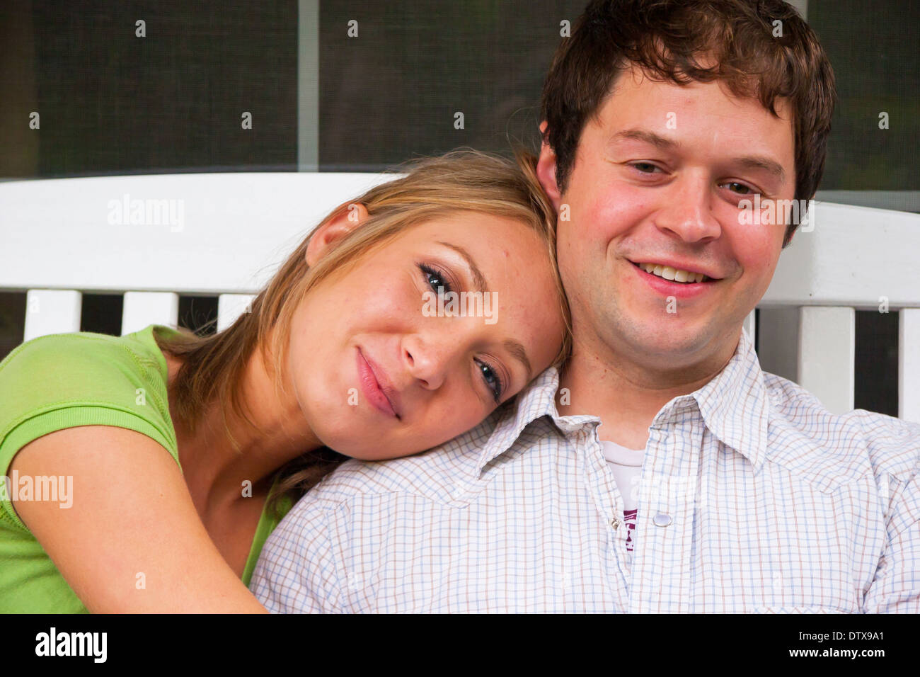 Engaged couple spending time together sitting on a porch with a white rocking chair. Stock Photo