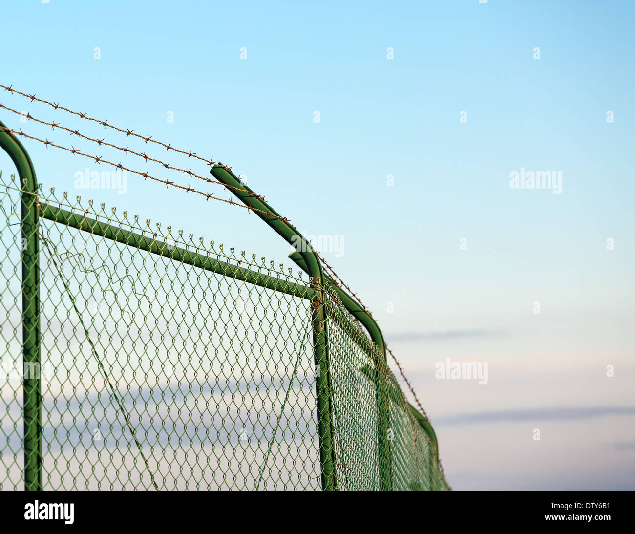 Mesh fence with barbed wire on a background of blue sky Stock Photo