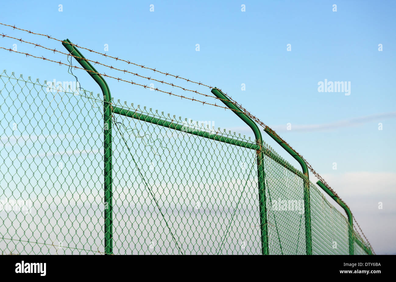 Mesh fence with barbed wire on a background of blue sky Stock Photo