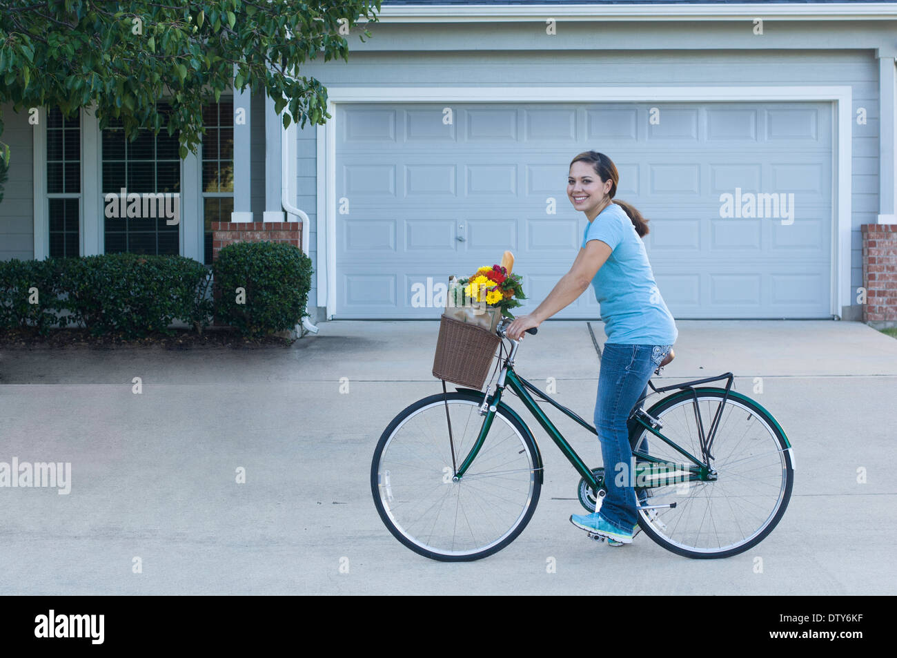 Mixed race woman riding bicycle in driveway Stock Photo