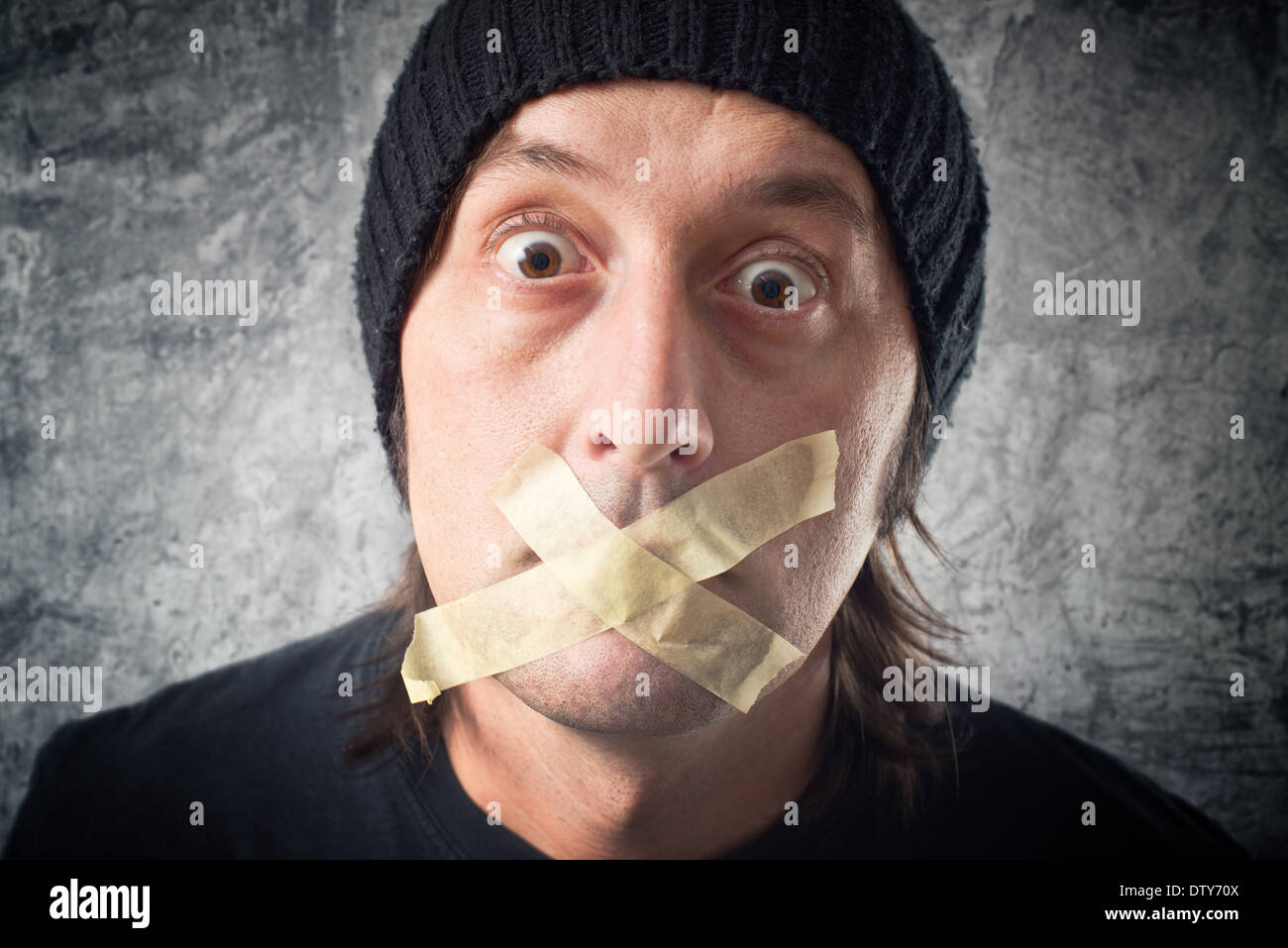 My lips are sealed. Casual Man with black cap having tape over his mouth. Stock Photo