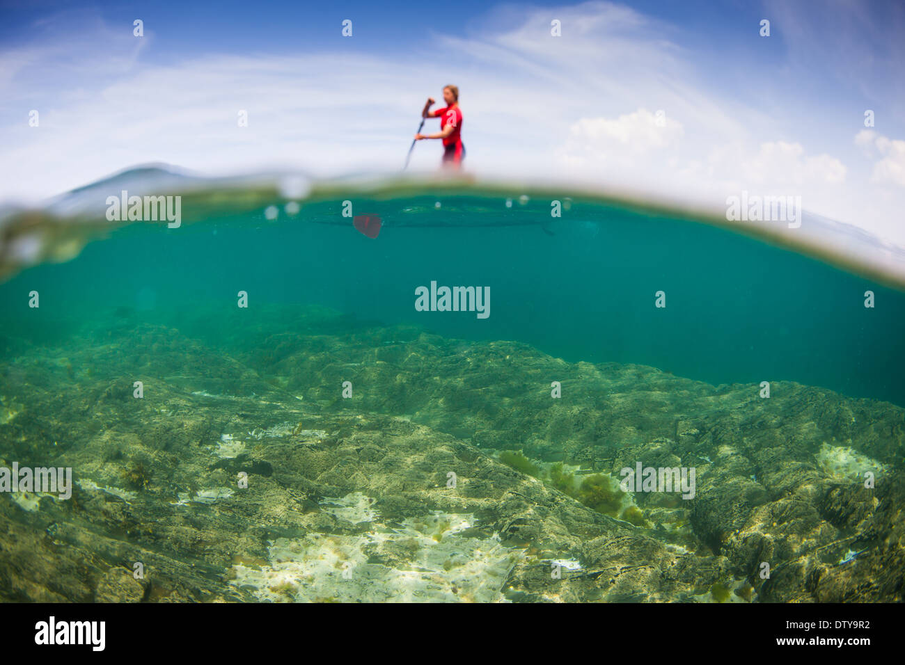 A girl in a red rash vest paddleboards in the clear waters of North
