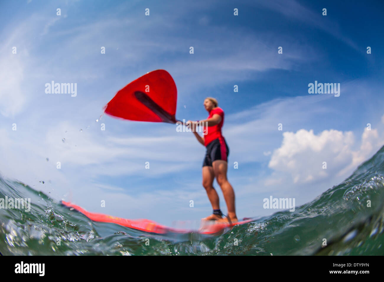 A girl in a red rash vest paddleboards in the clear waters of North Devon UK SUP (stand up paddleboarding) Stock Photo