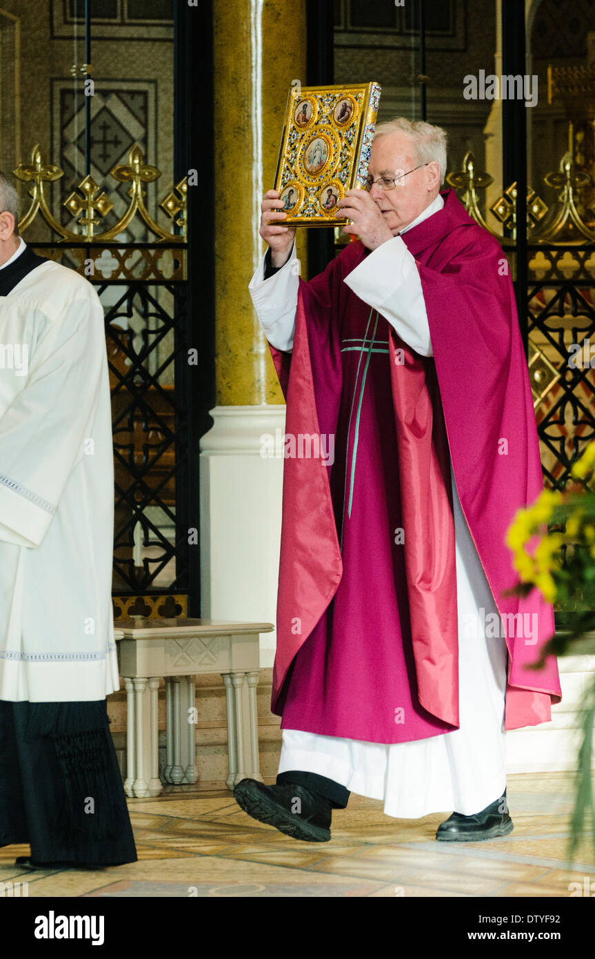 A bishop holds up a gold covered bible during a mass Stock Photo