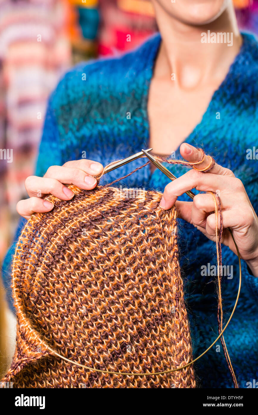 Young woman or saleswoman in knitting shop showing or explaining how to knit with circular needle Stock Photo