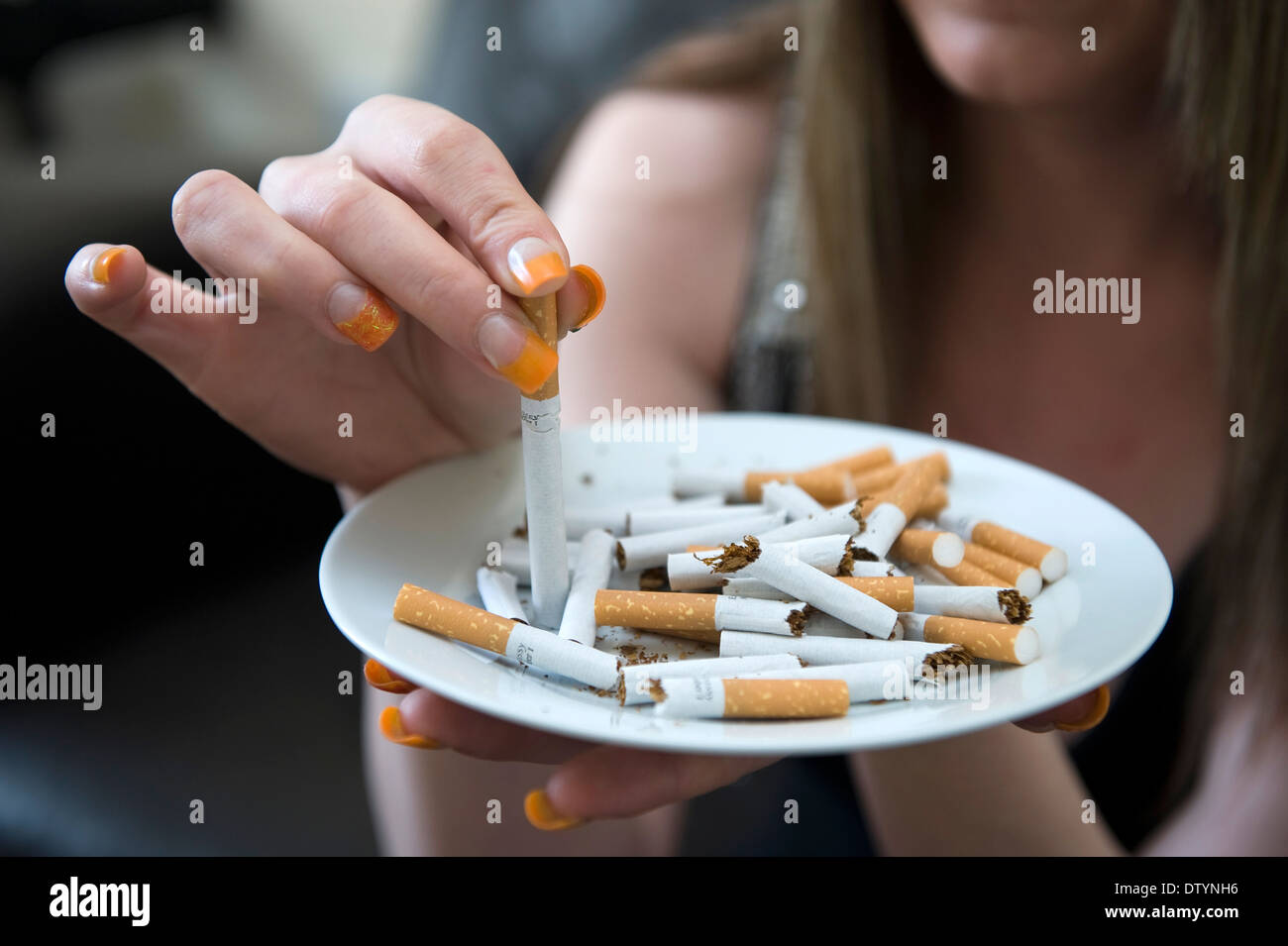 cigarette stubs A woman stubs a cigarette stub out in an ashtray of other cigarettes in an  attempt to quit smoking Stock Photo