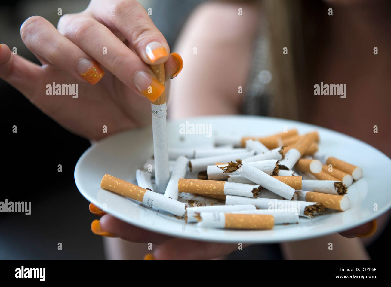 A woman stubs a cigarette stub out in an ashtray of other cigarettes in
