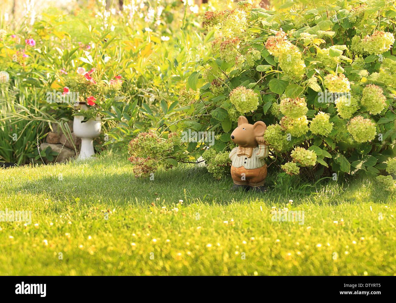 Figurine, clay mouse is on a well-kept lawn, green grass, next to a bush blooming hydrangeas. Sunny summer day. Stock Photo